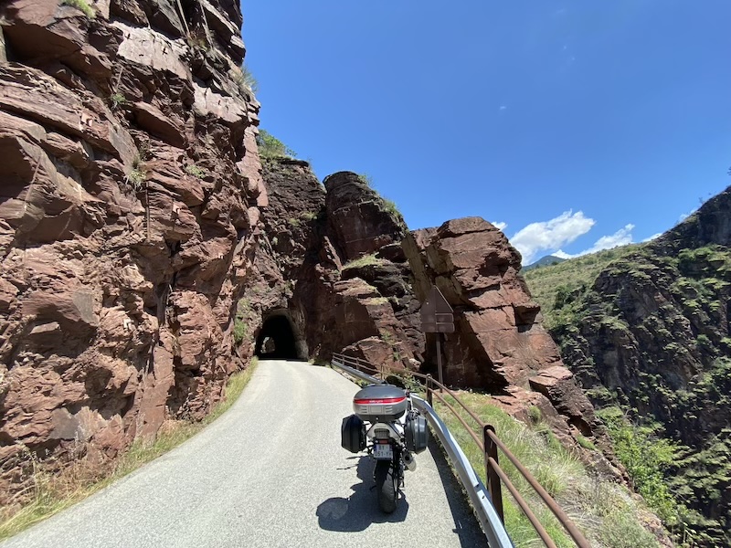 Moto de voyage chargée devant un tunnel creusé dans la roche sur une route de gorges